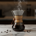 Glass pour over coffee server with wood collar, leather tie and stainless steel filter on marble surface